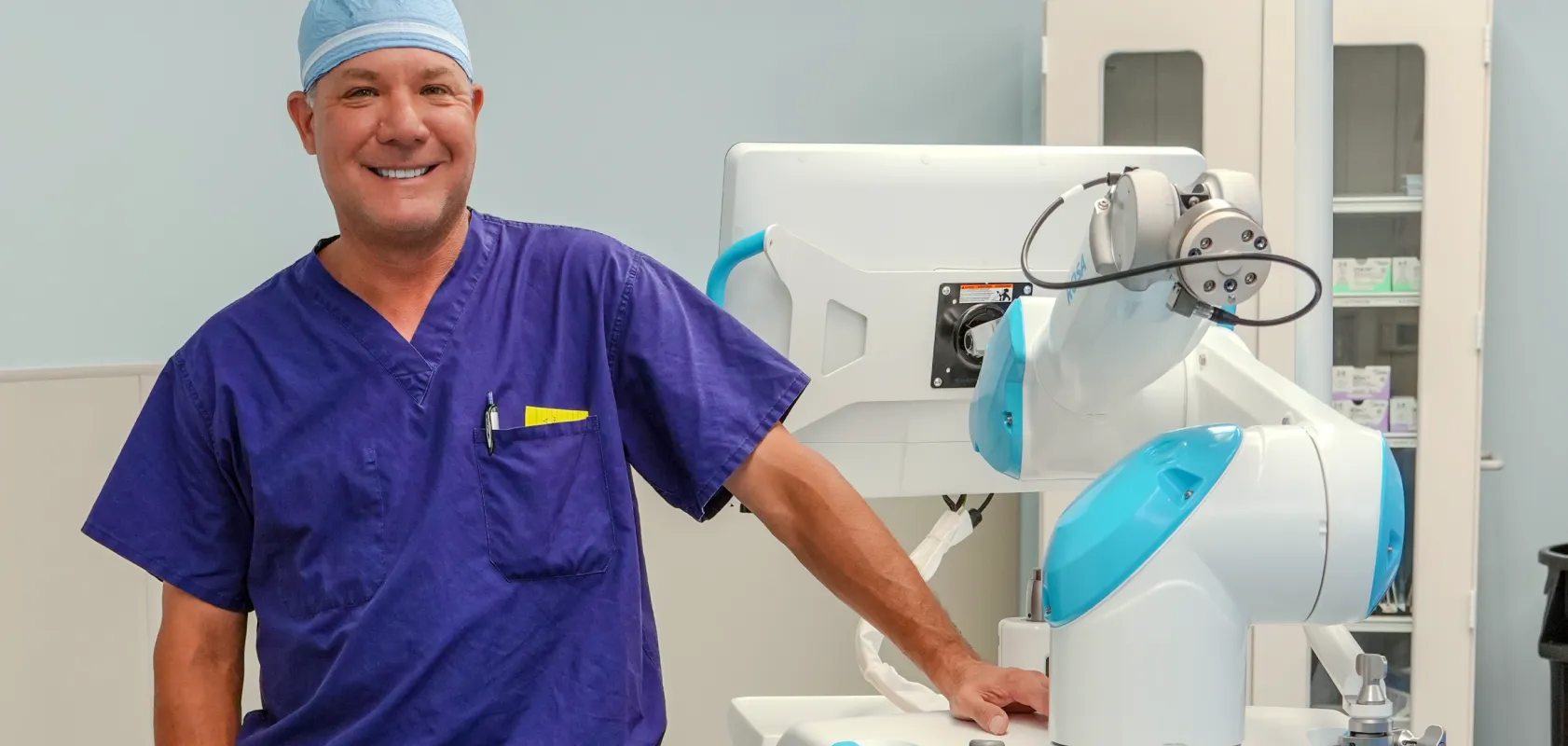 An OSS Health orthopedic surgeon in purple scrubs standing beside a robotic surgical system.