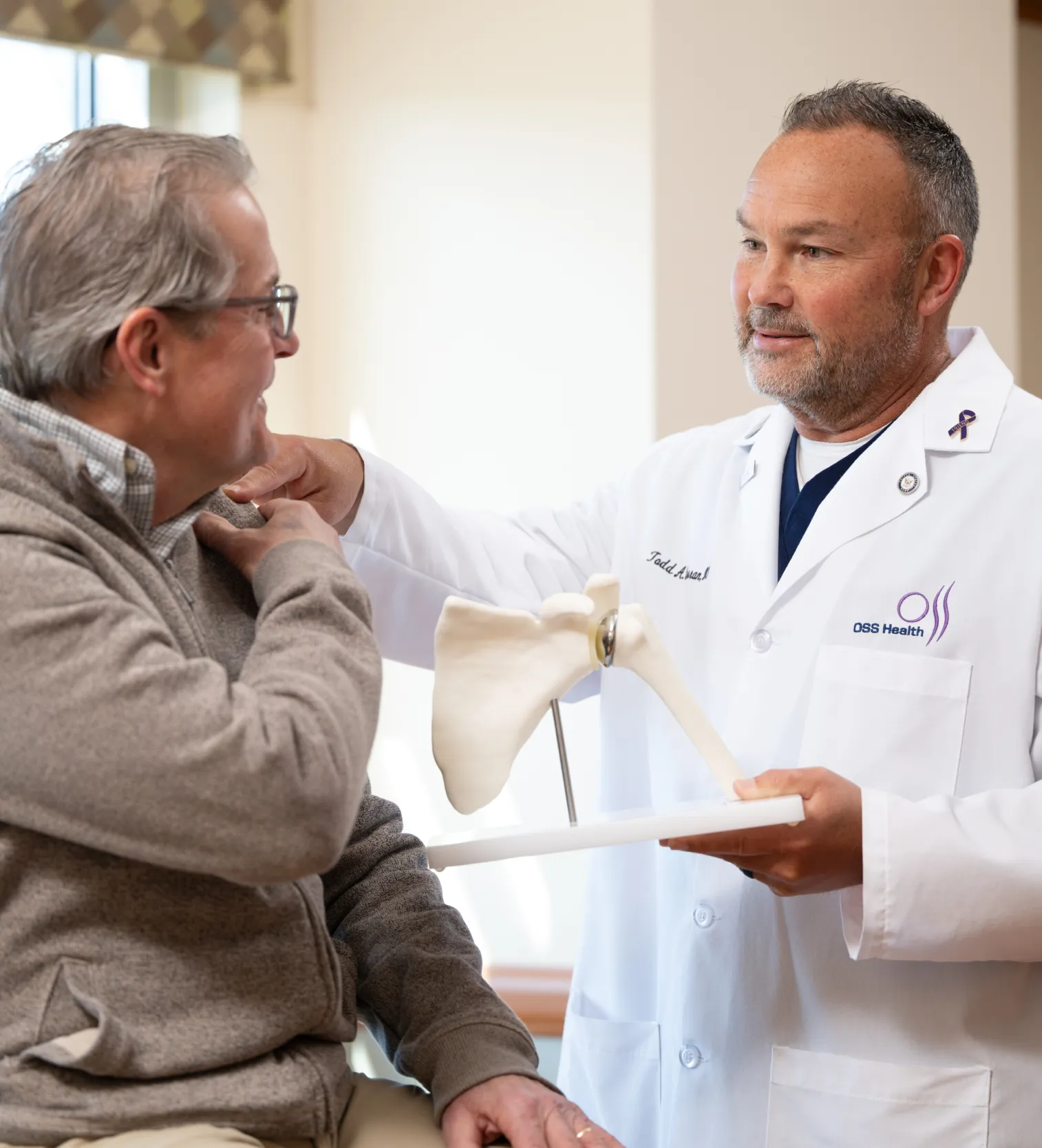 “OSS Health orthopedic specialist discusses shoulder treatment with a patient using a shoulder joint model.